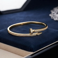 A gold hinged bangle bracelet with pavé-set clear stones, styled on a dark blue velvet jewelry box.