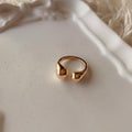 A gold-toned split ring with a textured, organic shape, resting on a white ceramic tray with a soft white faux fur background.