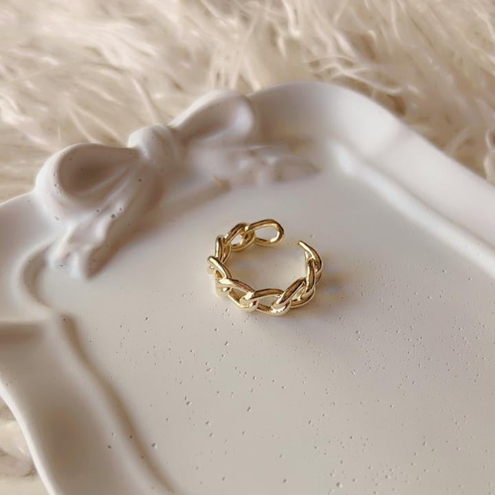 A delicate gold chain-link ring resting on a white ceramic tray with a bow detail, set against a soft beige faux fur background.
