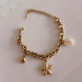 A gold-tone chain bracelet with dangling seashell and starfish charms, displayed on a white surface.