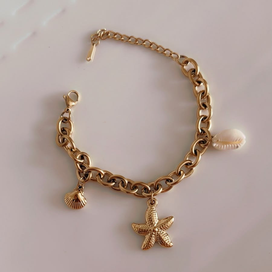 A gold-tone chain bracelet with dangling seashell and starfish charms, displayed on a white surface.